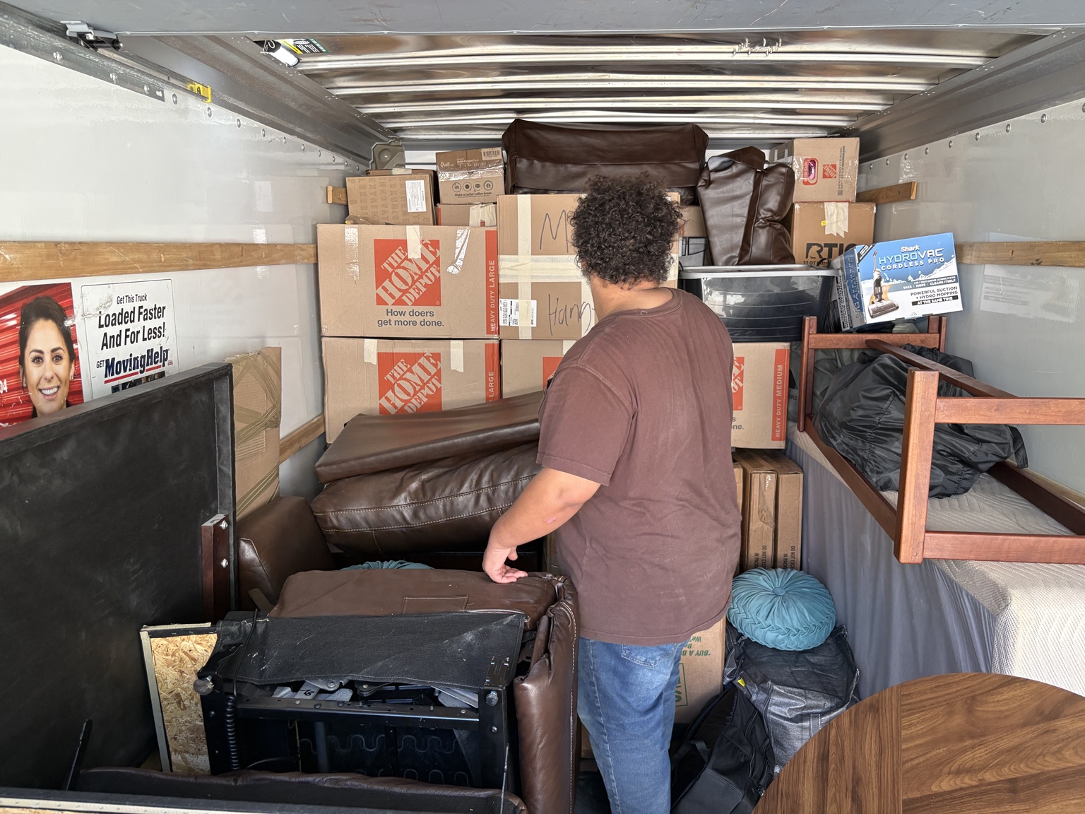 A person handling furniture inside a rental truck with packed boxes and household items.