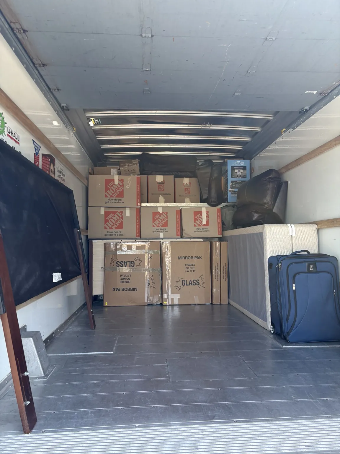 Stacked moving boxes, mirror cartons, a covered mattress and luggage inside a rental truck.
