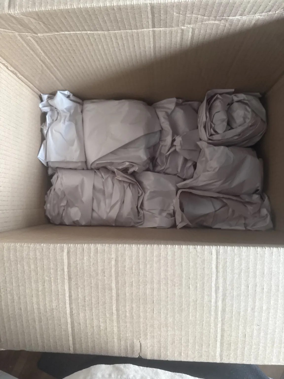 Paper-wrapped items arranged inside an open cardboard moving box