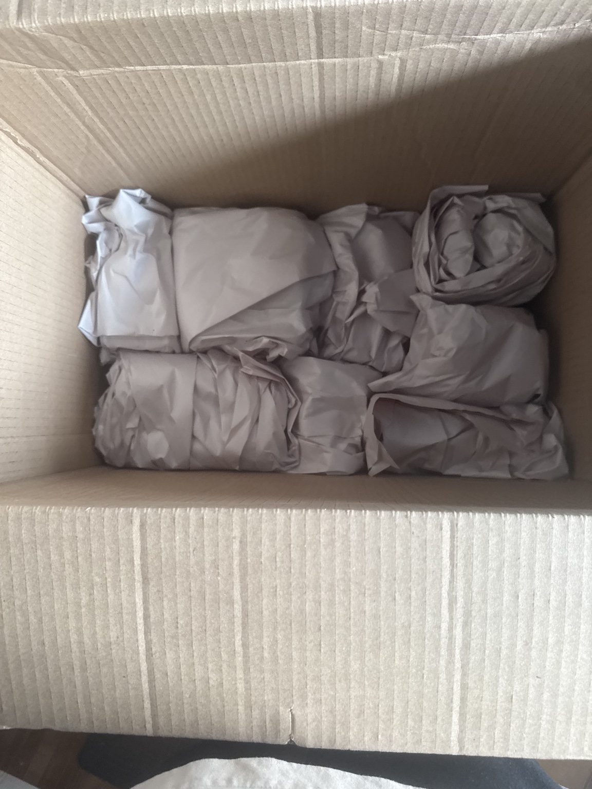 Paper-wrapped items arranged inside an open cardboard moving box